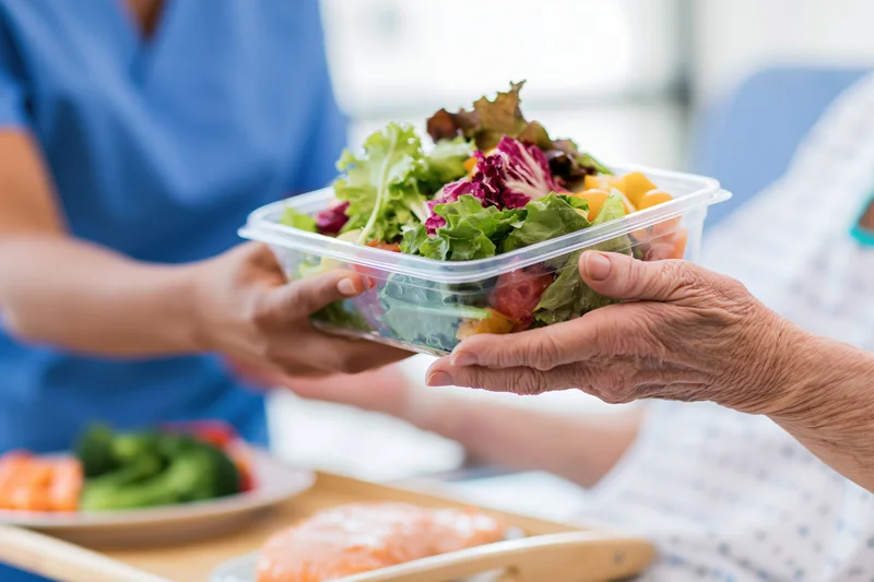 Nurse handing a salad container to a senior patient in a hospital setting