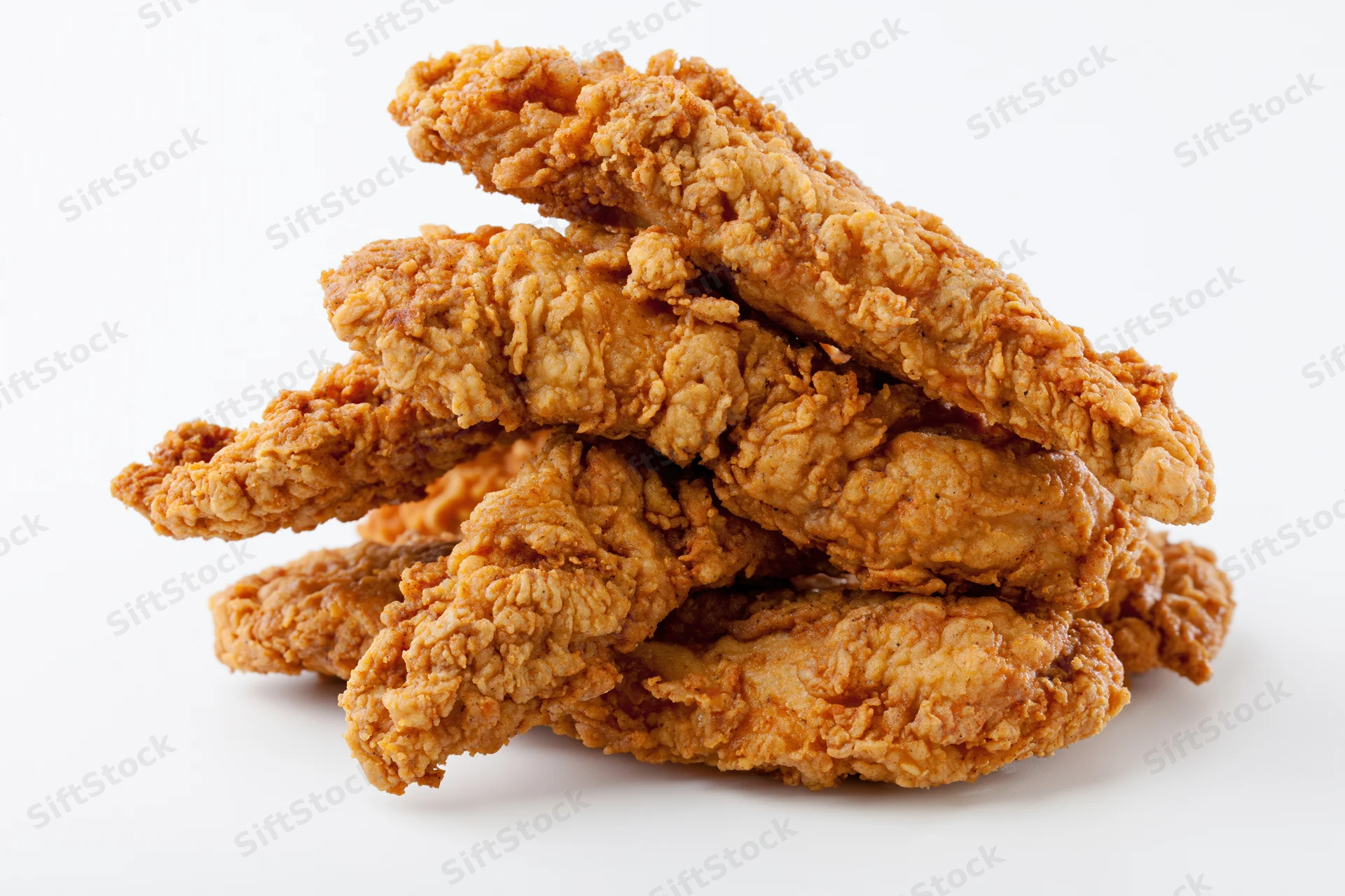 Pile of crispy fried chicken tenders stacked loosely on white background