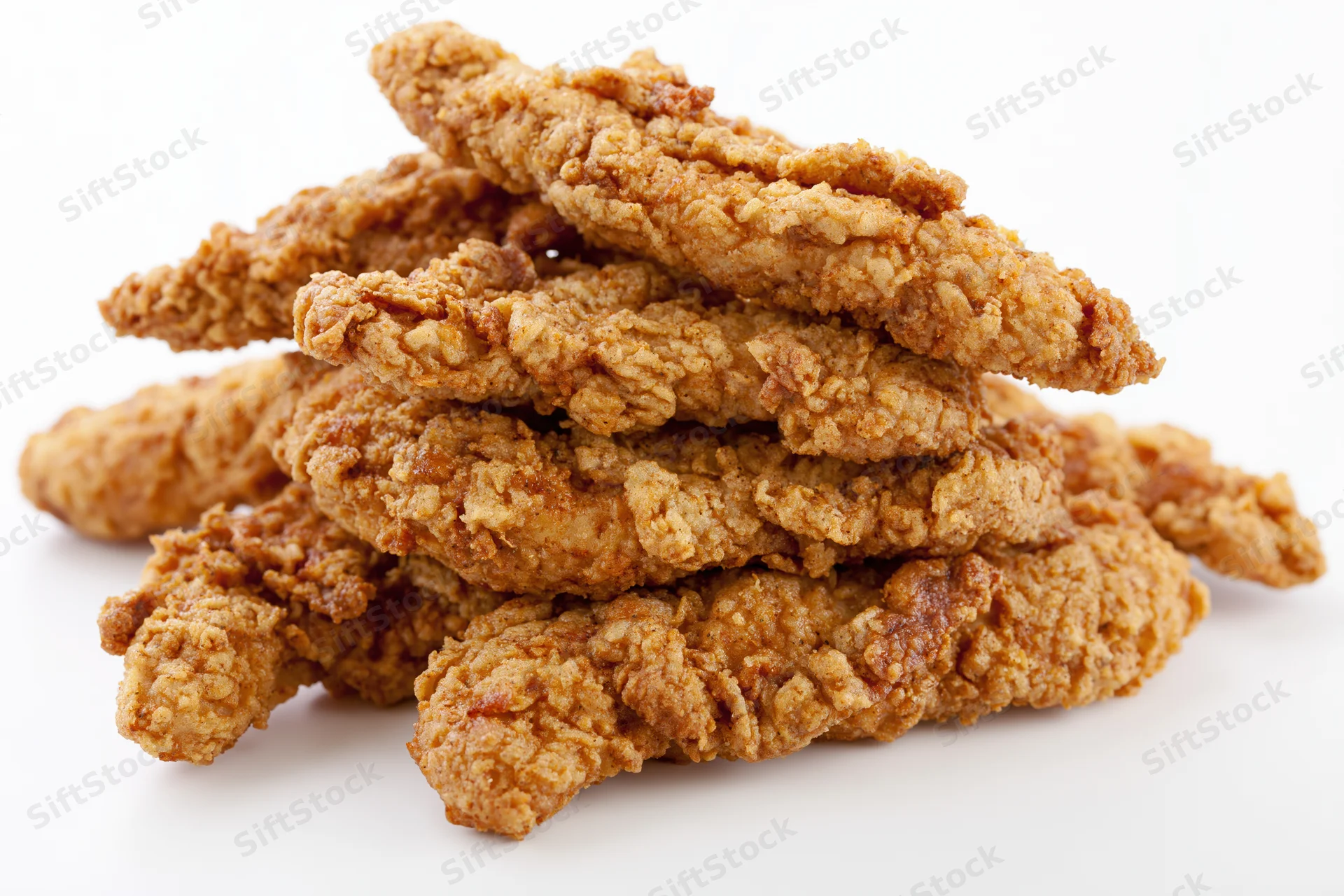 Crispy fried chicken tenders stacked loosely on white background