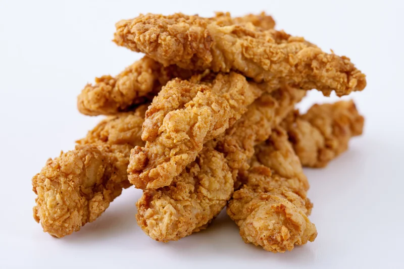 Crispy fried chicken tenders piled loosely on white surface