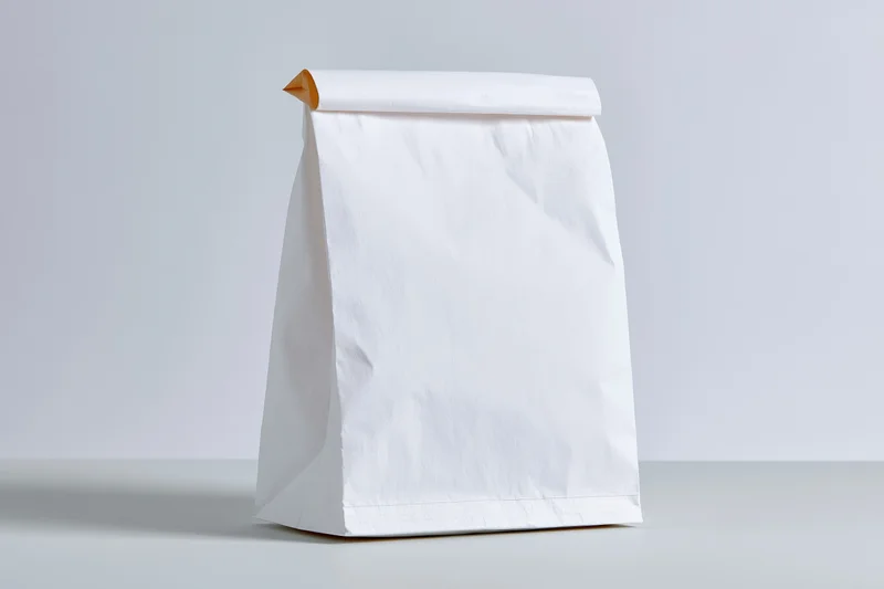 Plain white paper bag standing upright on a flat surface with copyspace for branding