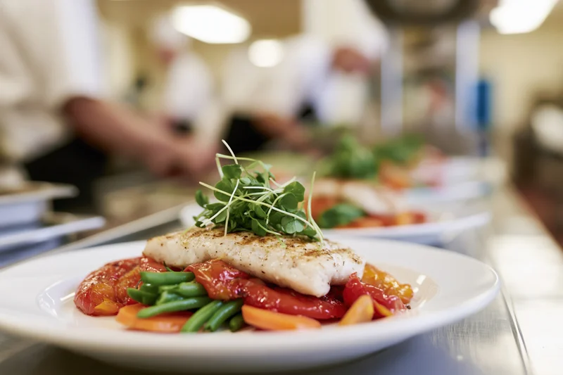 Grilled fish fillet topped with microgreens on a plate in a restaurant kitchen