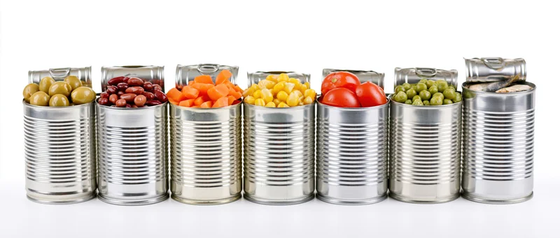 Row of open metal cans filled with various canned vegetables and sardines on white background