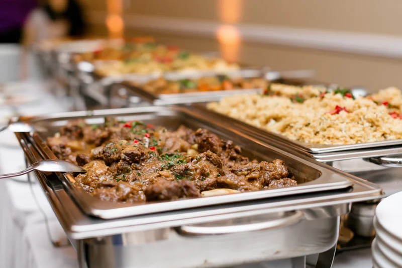 Row of stainless steel chafing dishes filled with hot catered food on a buffet table