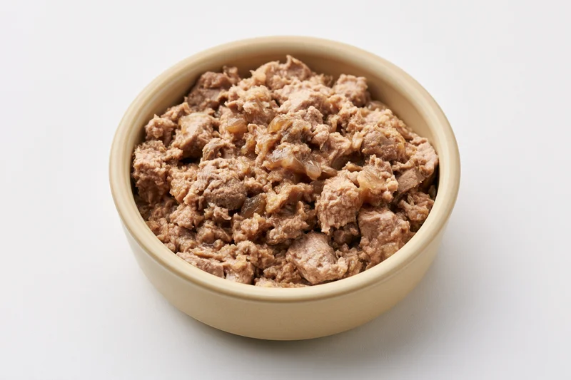 Chunky wet cat food in a small beige ceramic bowl on white background
