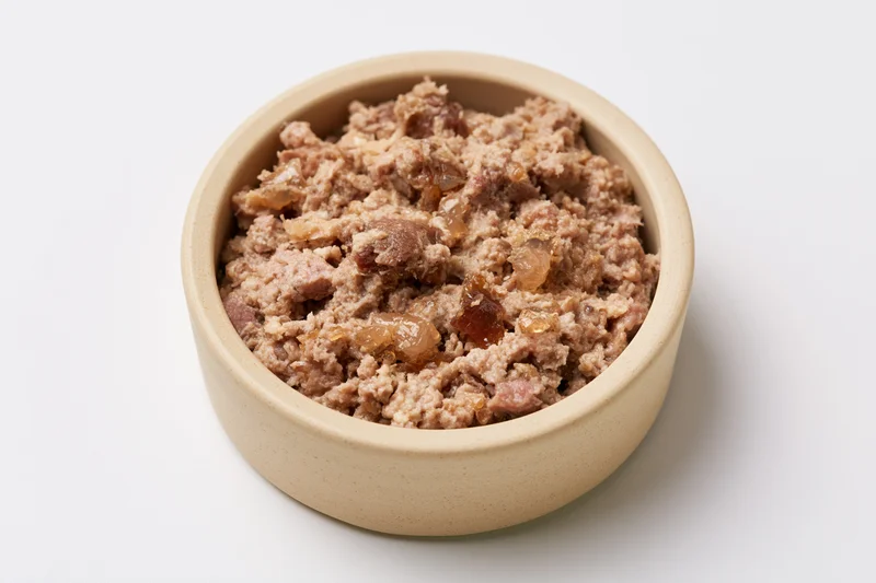 Chunky wet cat food in a small beige ceramic bowl on white background