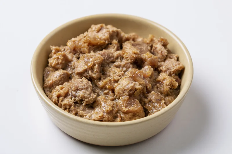Chunky wet cat food in a small beige ceramic bowl on white background