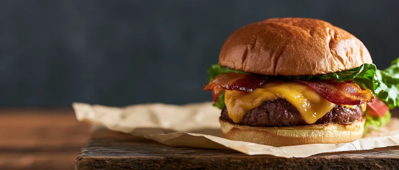 Thick bacon cheeseburger with melted cheddar and crispy bacon on a wooden board with parchment paper