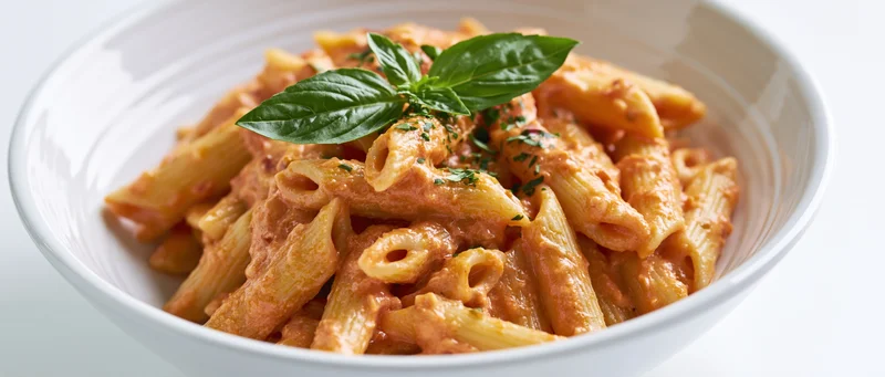 Penne pasta in creamy tomato sauce served in a white ceramic bowl with fresh basil garnish