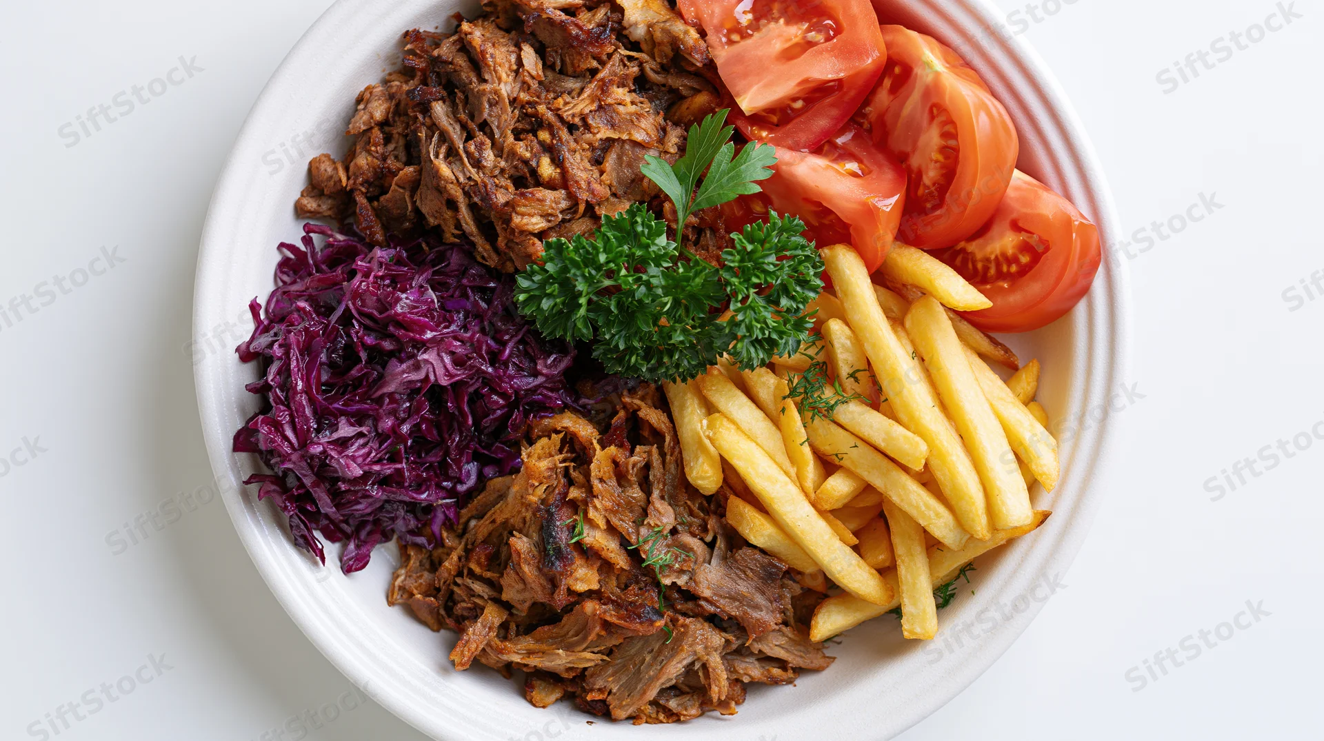 Shredded kebab meat with fries, tomatoes, and red cabbage on a white plate, top view
