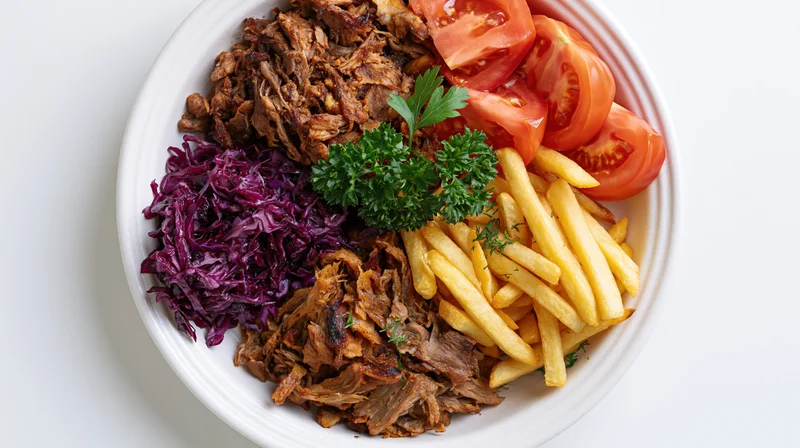 Shredded kebab meat with fries, tomatoes, and red cabbage on a white plate, top view