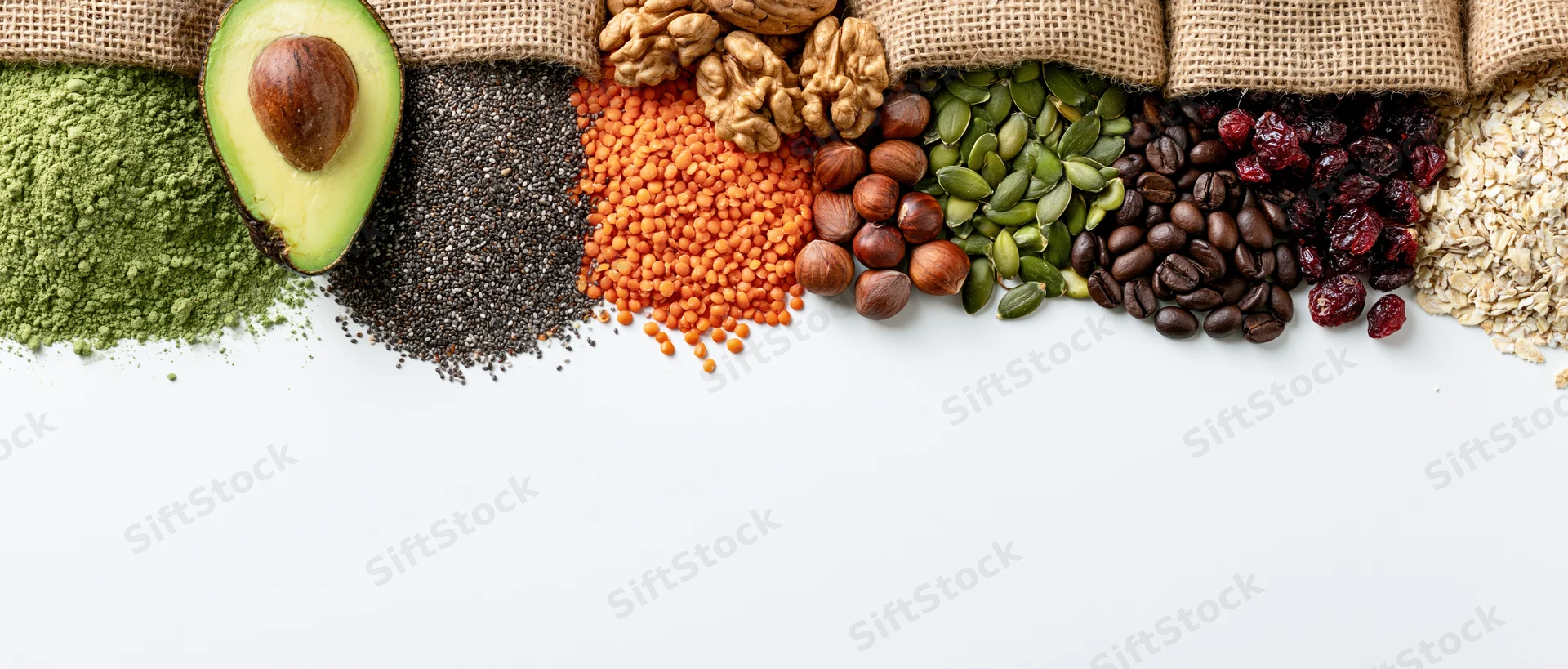 A row of superfoods and whole ingredients arranged in burlap sacks on white background with copyspace below