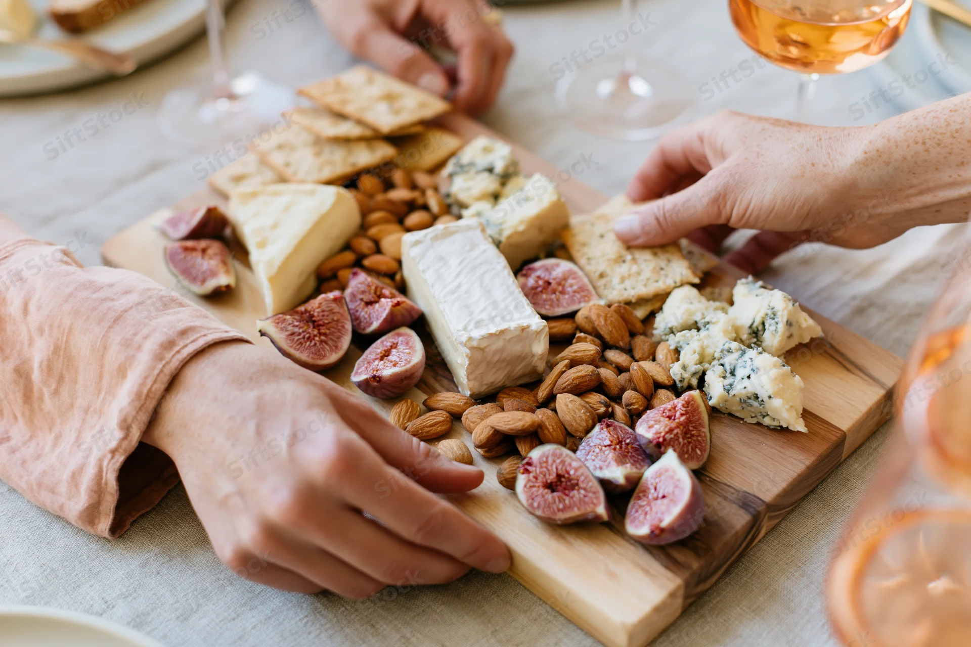 Woman’s hands arranging a wooden charcuterie board with cheese, figs, almonds and wine on a table