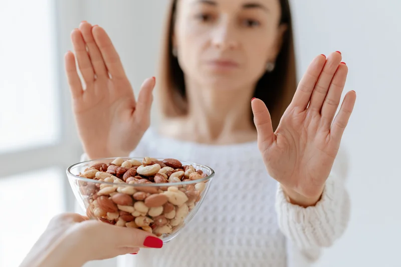 Woman pushing away glass bowl of mixed nuts with hands raised in refusal
