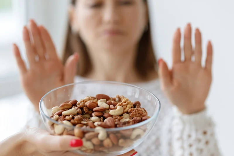 Woman pushing away a glass bowl of mixed nuts with hands raised in refusal