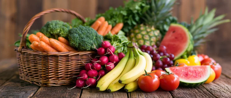 Abundant fresh fruits and vegetables arranged in a wicker basket on a wooden table