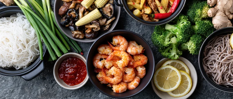 Shrimp and vegetables arranged with noodles and sauce on dark stone surface