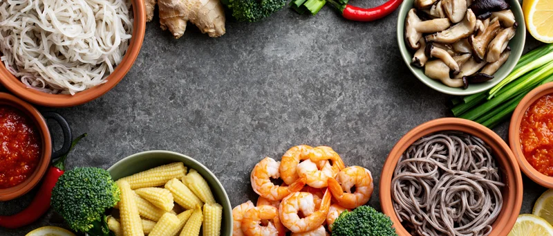 Asian cooking ingredients arranged around the border of a gray countertop with copyspace in center