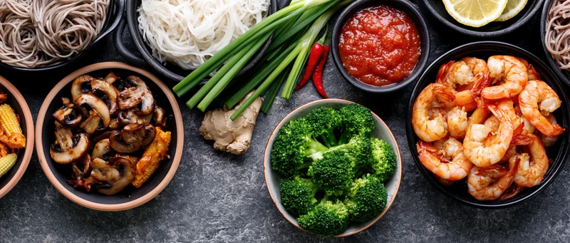 Various asian cooking ingredients arranged in bowls around a dark surface in a flat lay overhead view