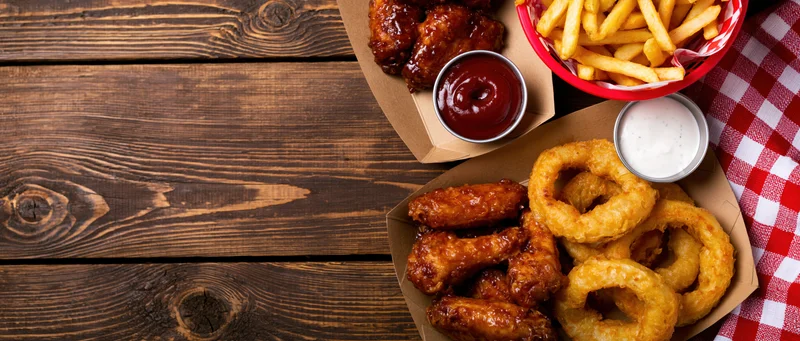 Bar food spread with wings, onion rings and fries on wooden table with checkered cloth and copyspace