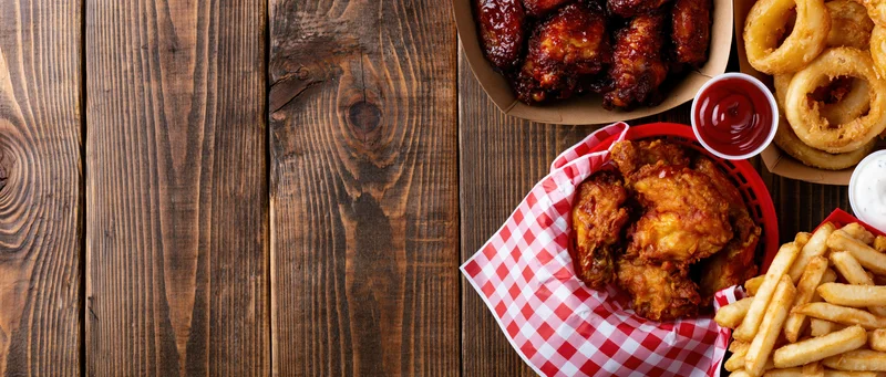 Assorted bar food including fried chicken, wings, onion rings and fries served in baskets on a wooden table with copyspace on the left