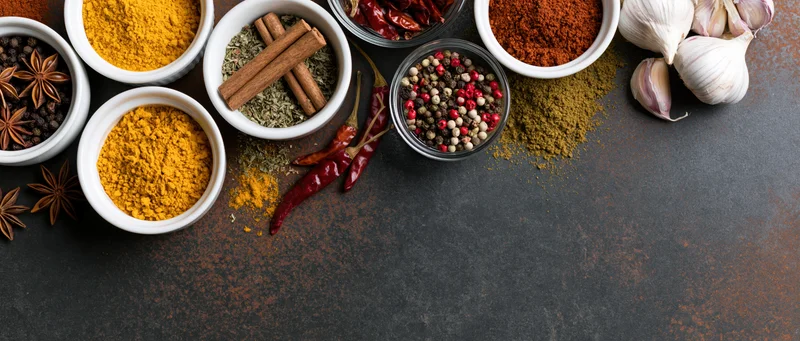 Assorted cooking spices arranged on dark rusted metal surface with copyspace