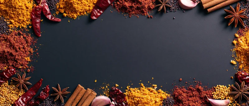 Dried spices arranged in a border around a dark surface with copyspace in the center