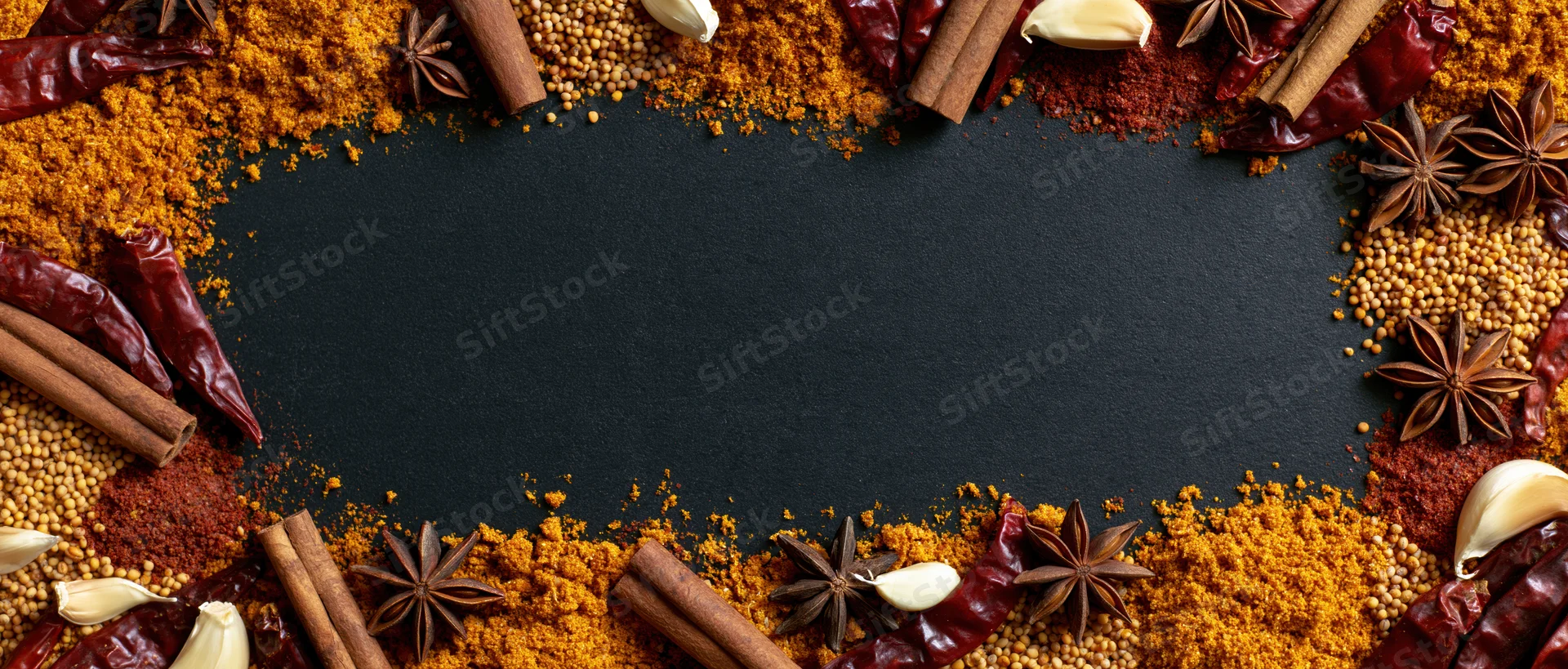 Assorted dried spices arranged in a border around a black surface with copyspace in the center