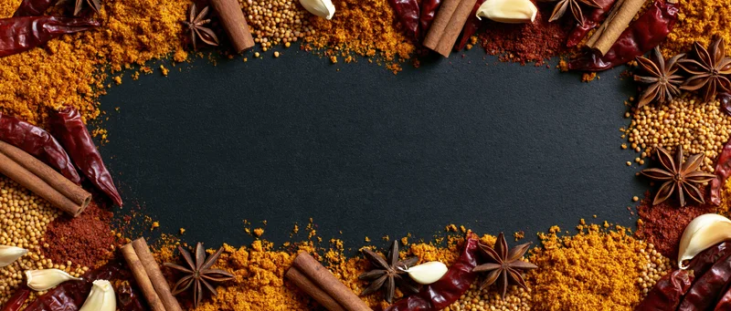 Assorted dried spices arranged in a border around a black surface with copyspace in the center