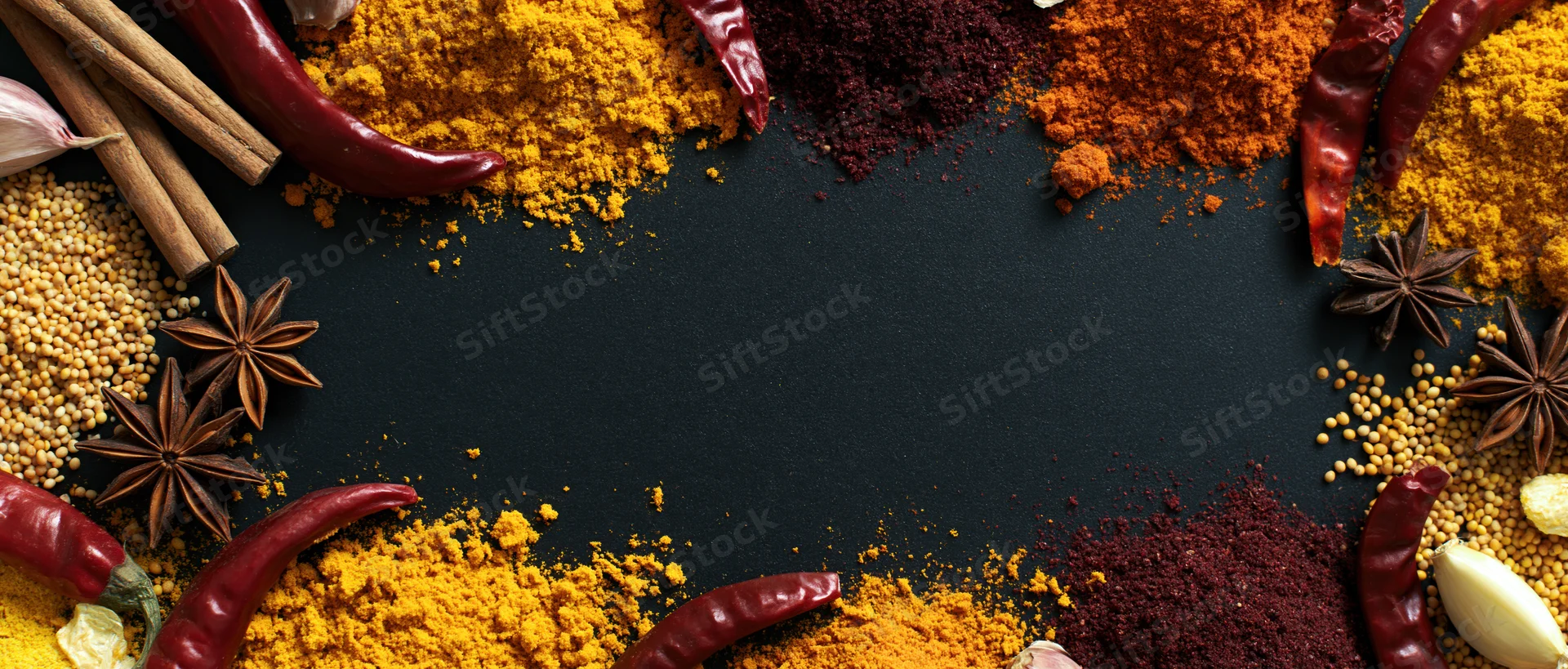 Dried spices arranged in a border around a dark surface with copyspace in center