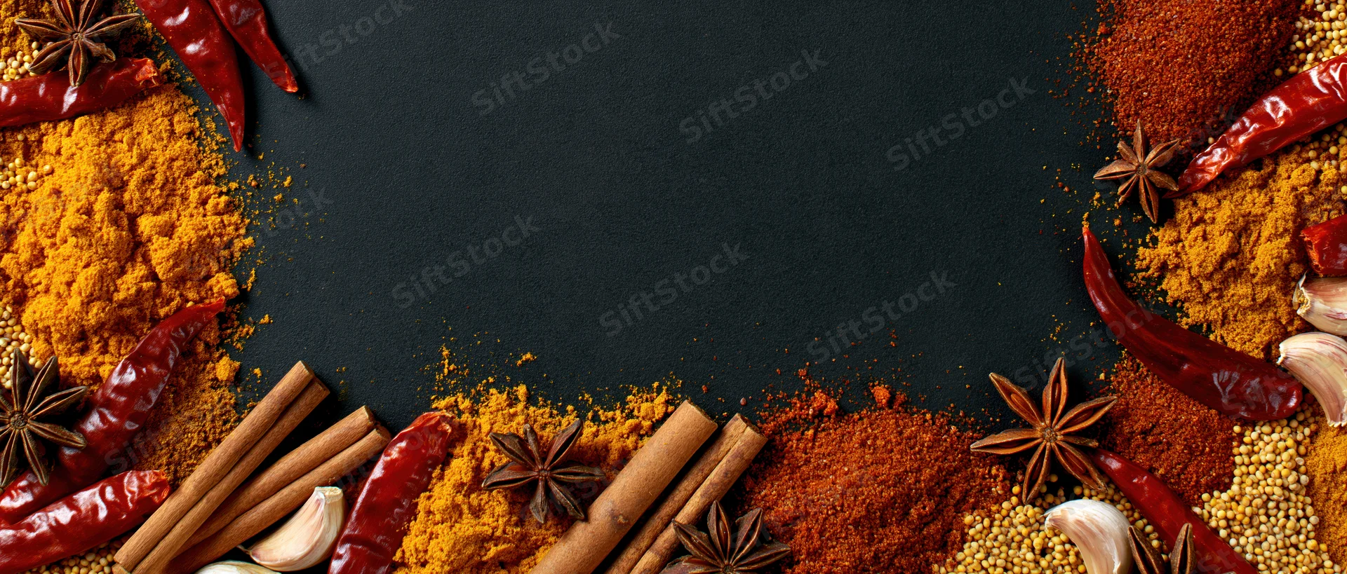 Assorted dried spices arranged in a border around a black surface with copyspace in center