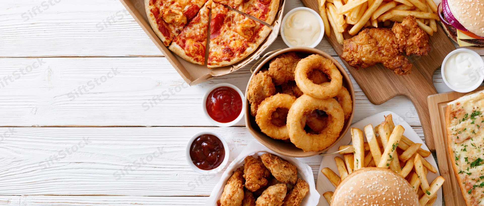 Assorted fast food items arranged along the left edge of a white wooden table with copyspace on the right