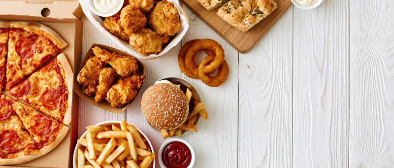Assorted fast food items arranged along the left side of a white wooden table with copyspace on the right