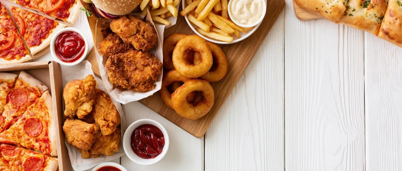 Assorted fast food items arranged along left side of white wooden table with copyspace on right