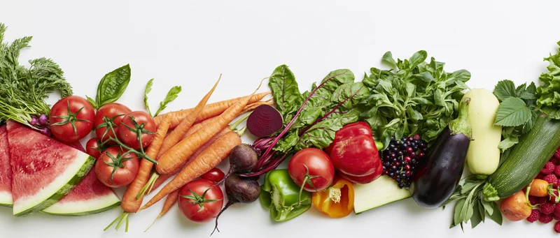 Assorted fresh vegetables and fruits arranged in a row on white background