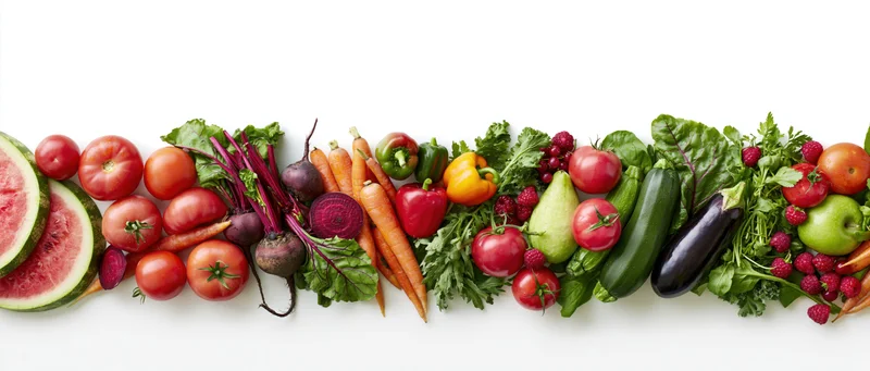 Assorted fresh fruits and vegetables arranged in a row on a white background