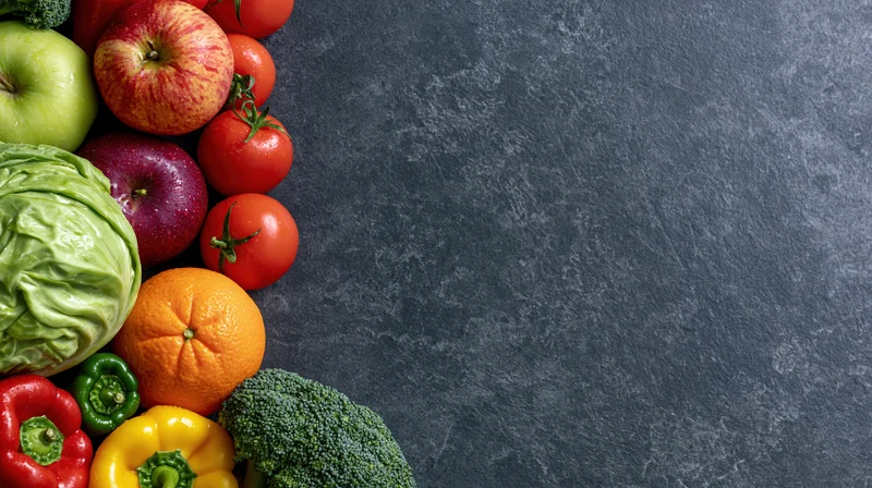 Fresh vegetables and fruits arranged along the left side of a dark slate surface