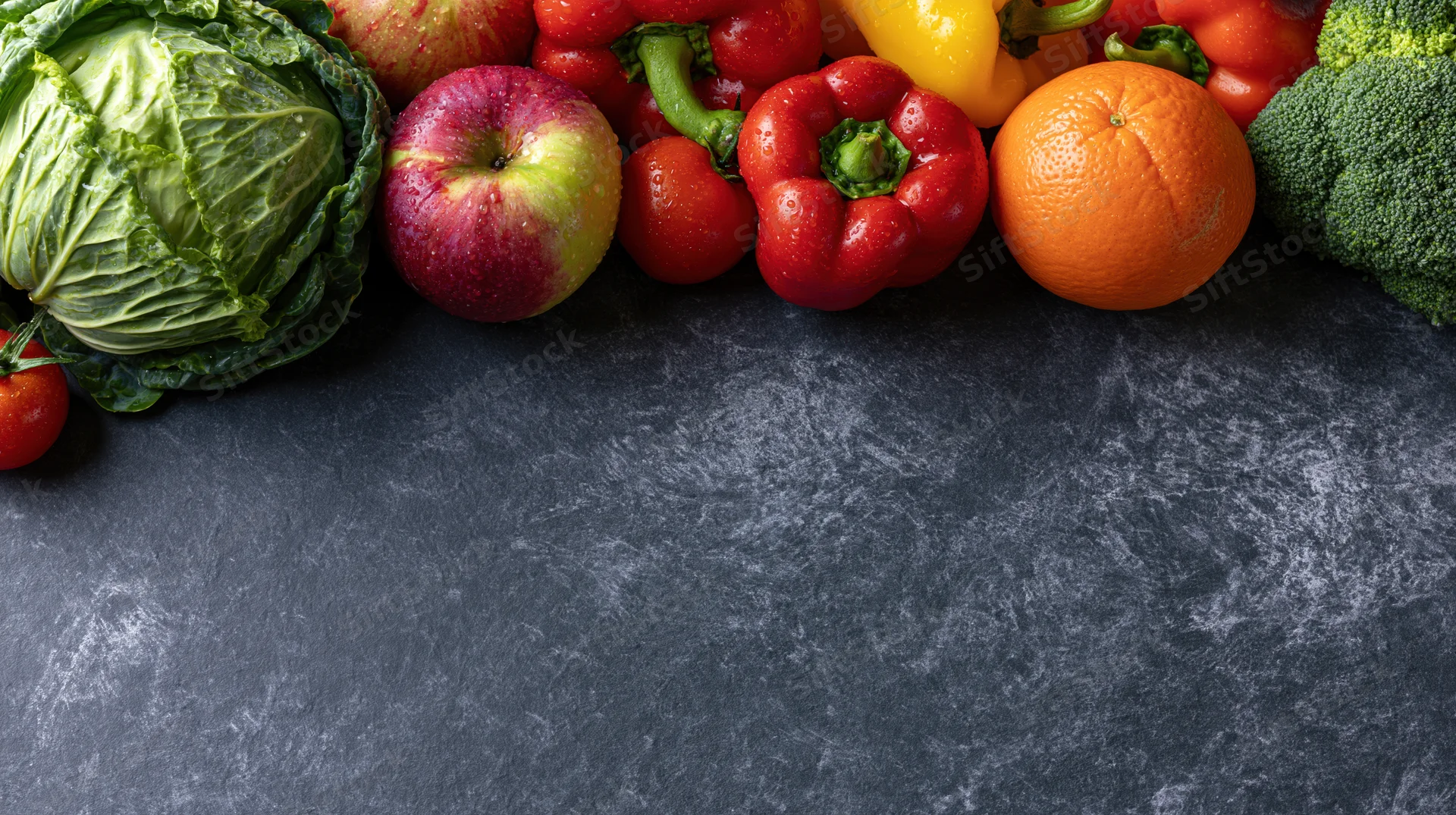 Fresh fruits and vegetables arranged along the top edge of a dark stone countertop