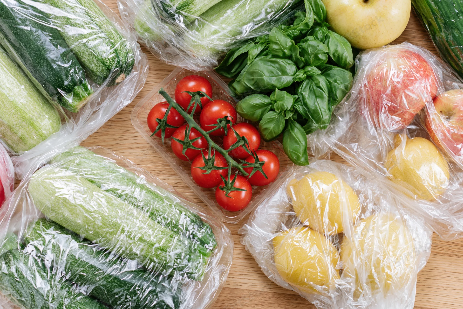 Fresh vegetables and fruits wrapped in clear plastic on wooden surface