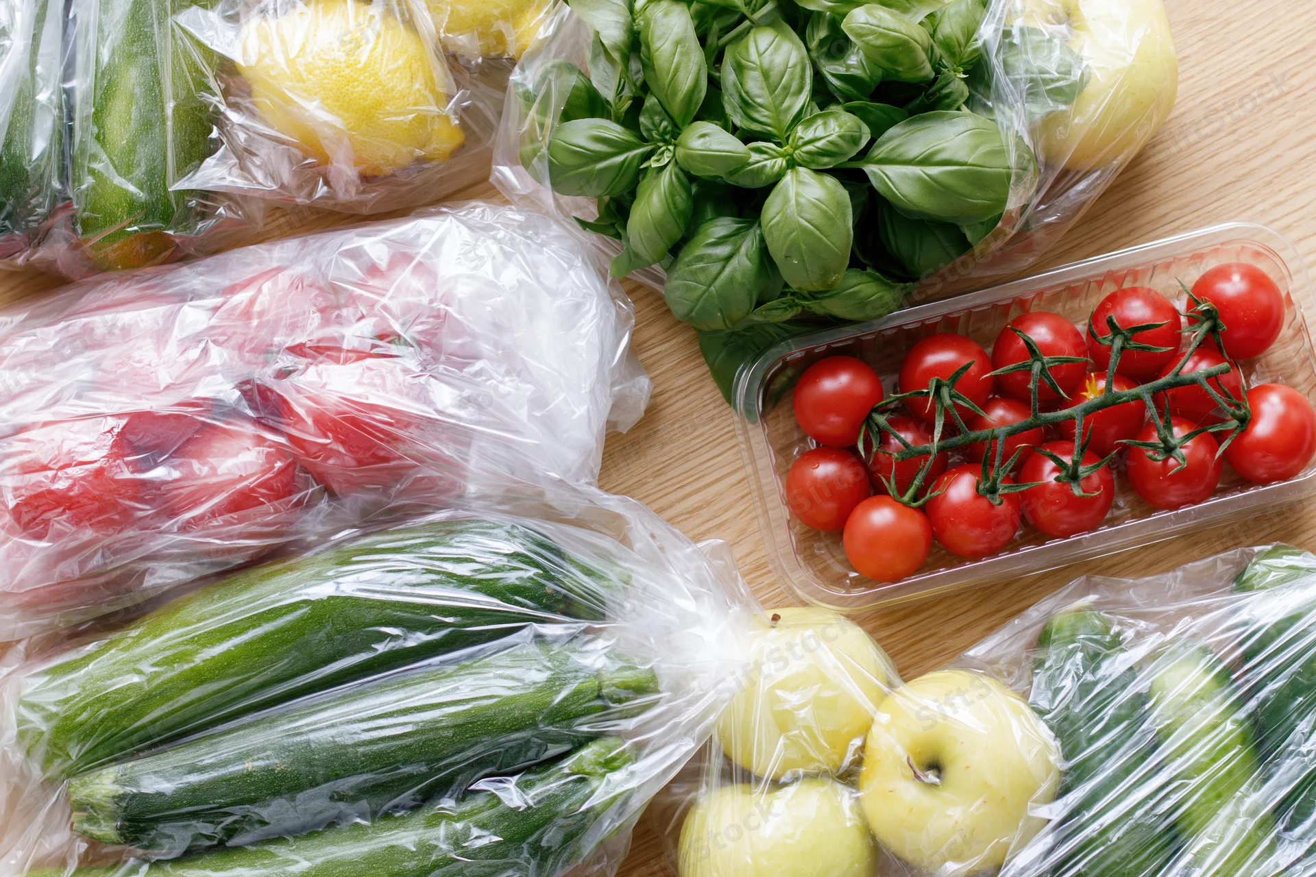 Assorted fresh vegetables and fruits wrapped in clear plastic on wooden countertop