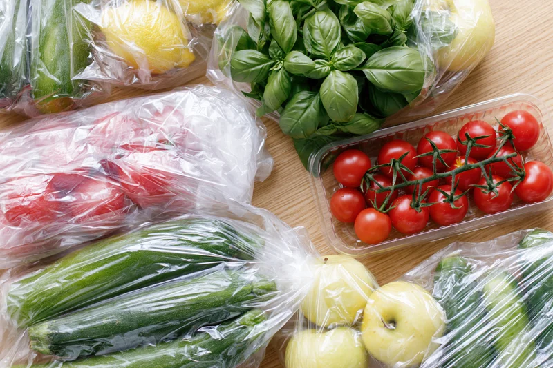 Assorted fresh vegetables and fruits wrapped in clear plastic on wooden countertop