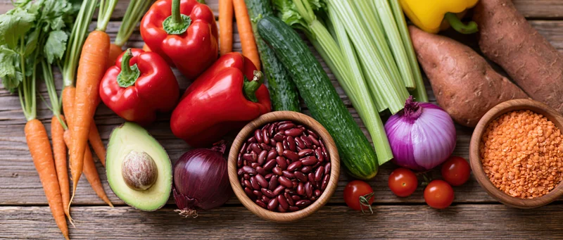 Fresh vegetables and legumes arranged on a wooden table in a flat lay composition
