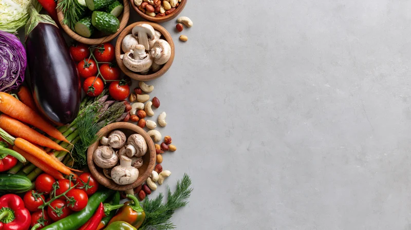 Fresh vegetables and nuts arranged along the left edge on a gray surface with copyspace