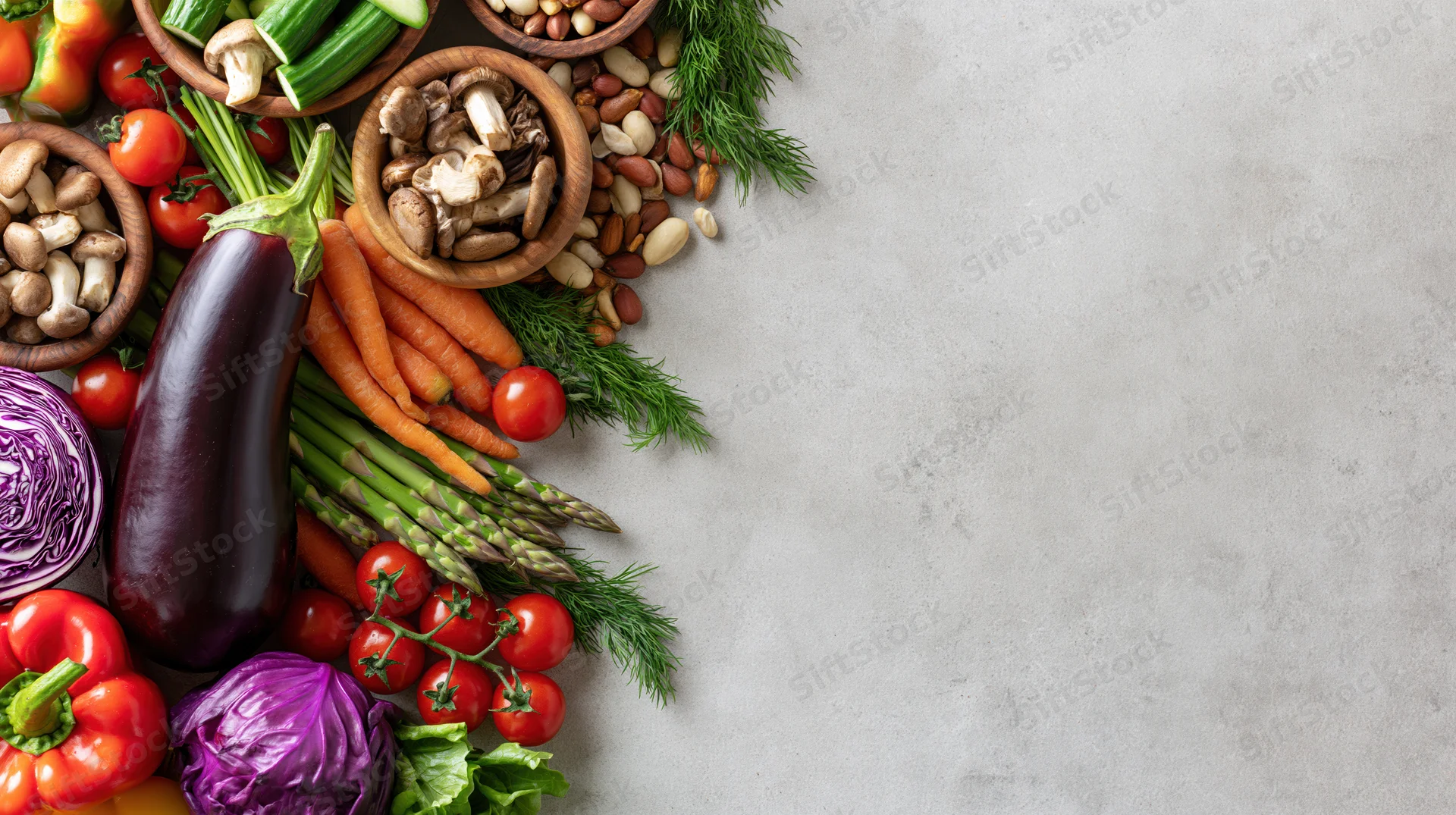 Fresh vegetables and nuts arranged along the left edge of a gray stone surface with copyspace on the right