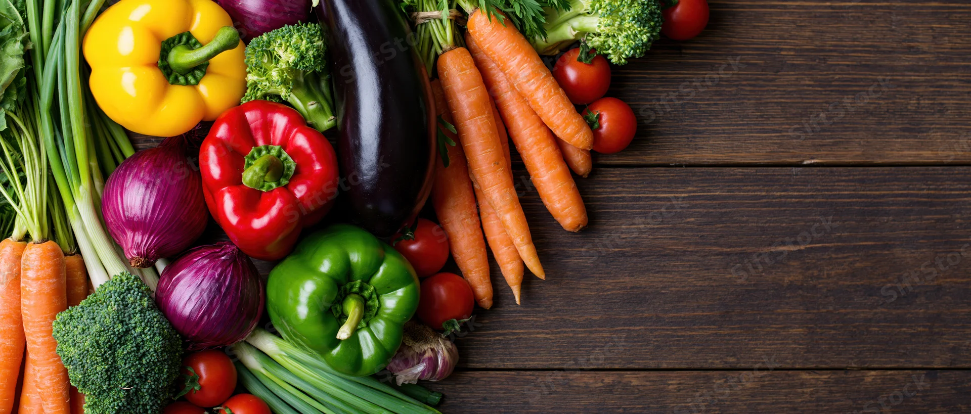 Fresh vegetables arranged in a loose pile along the left side of a dark wooden table, leaving copyspace on the right