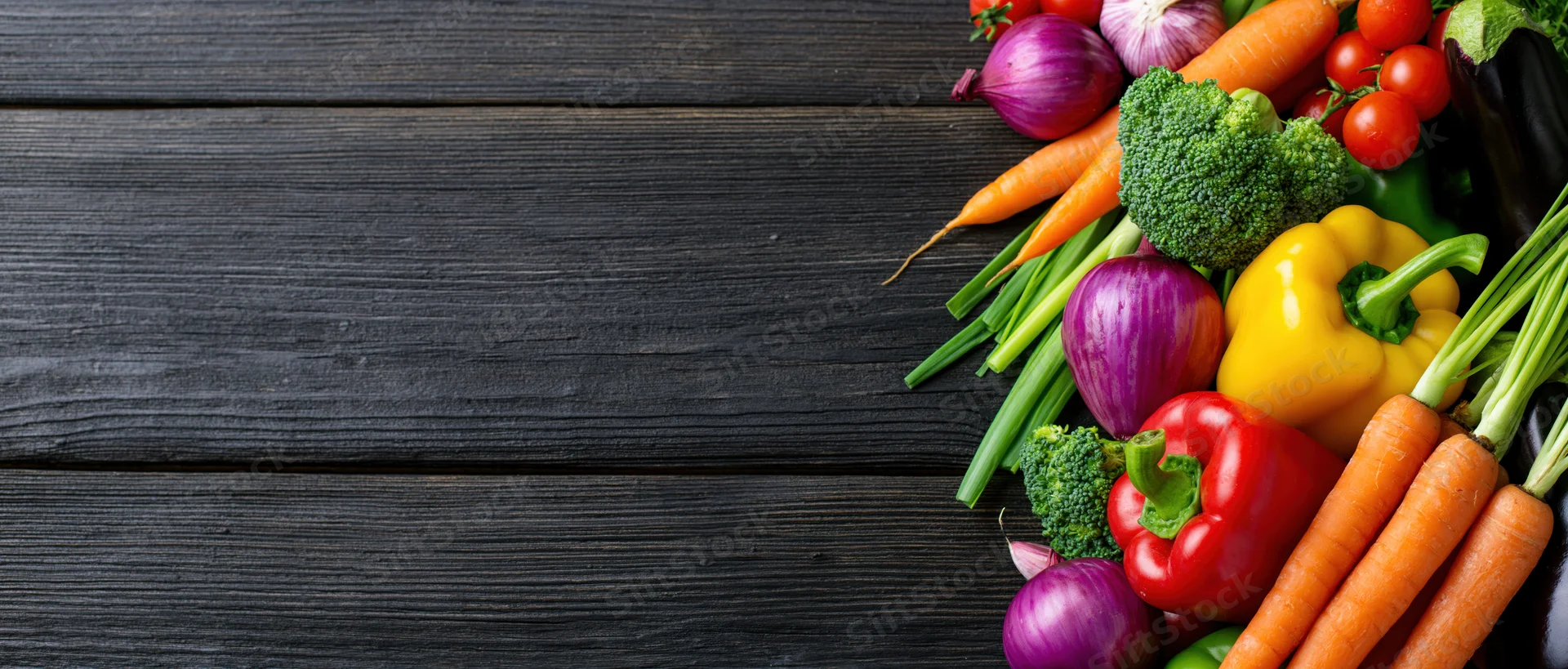 Fresh vegetables arranged in a loose pile along the right side of a dark wooden table