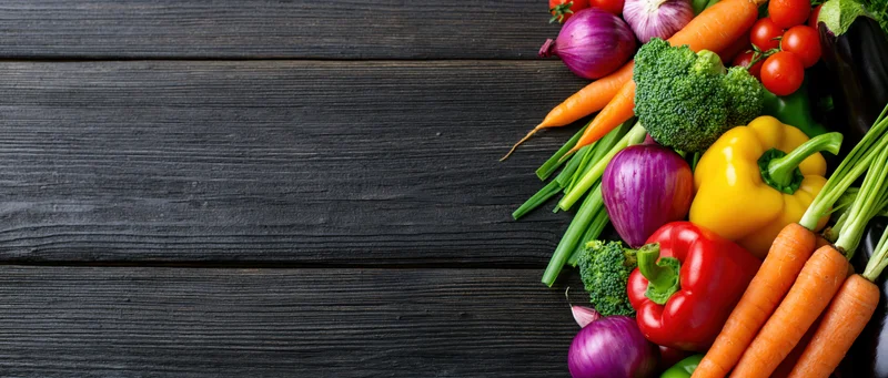 Fresh vegetables arranged in a loose pile along the right side of a dark wooden table
