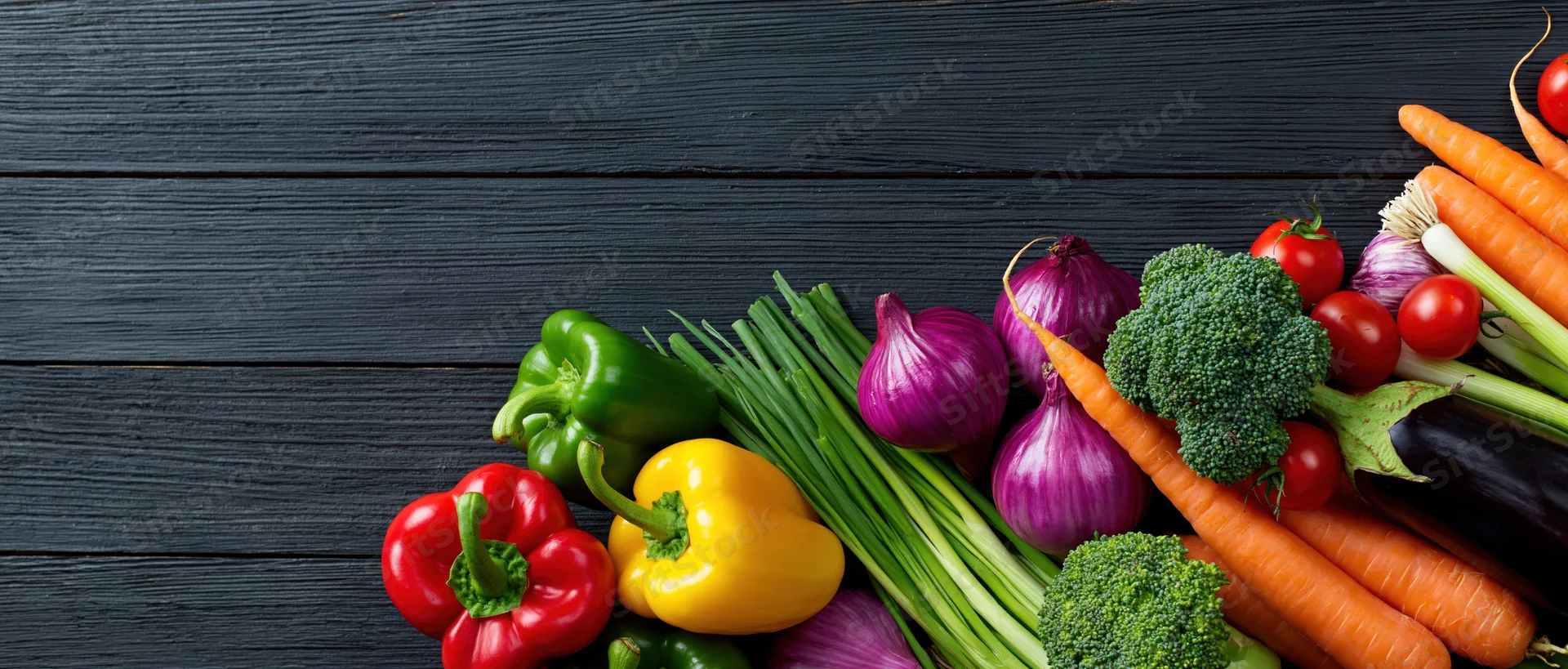 Assorted fresh vegetables arranged in a loose pile along the bottom right of a dark wooden surface