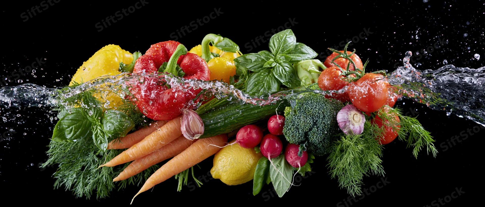 Fresh vegetables arranged in a row with water splashing over them on a black background