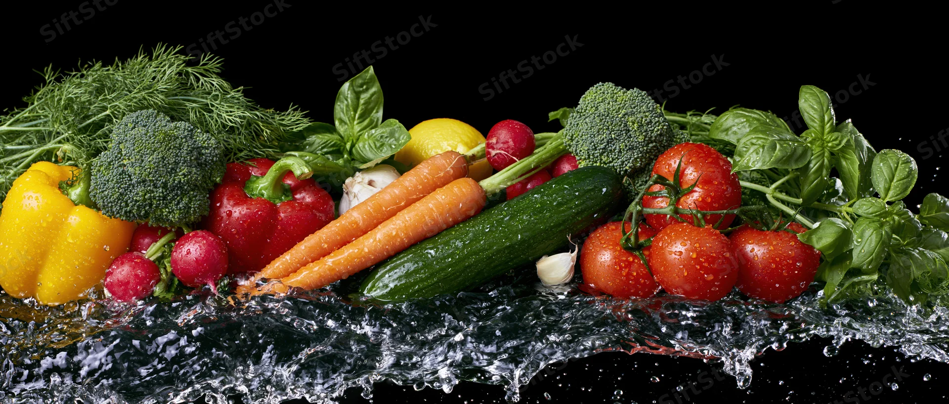 Fresh vegetables arranged in a row with water splashing around them on a black background